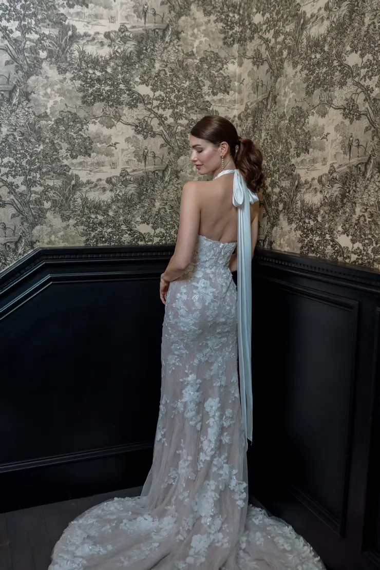 Model is wearing a wedding dress with a halter neckline and sequins and a back tied neck sash
