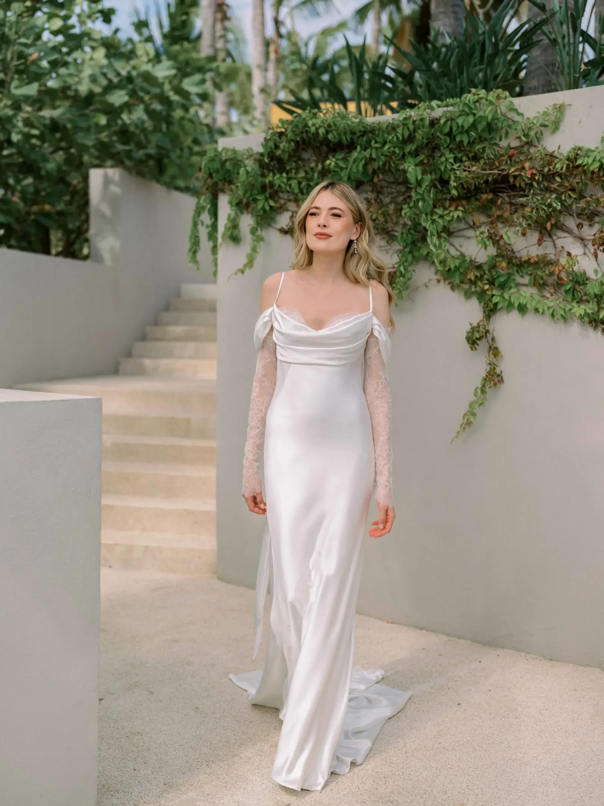 model is wearing a sleek minimalist off the shoulder satin sheath wedding dress