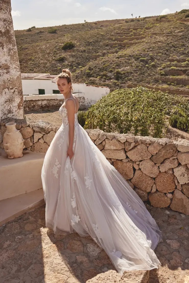 Model is wearing a wedding dress with a bikini neckline, beaded lace appliques, and a tulle chapel length train