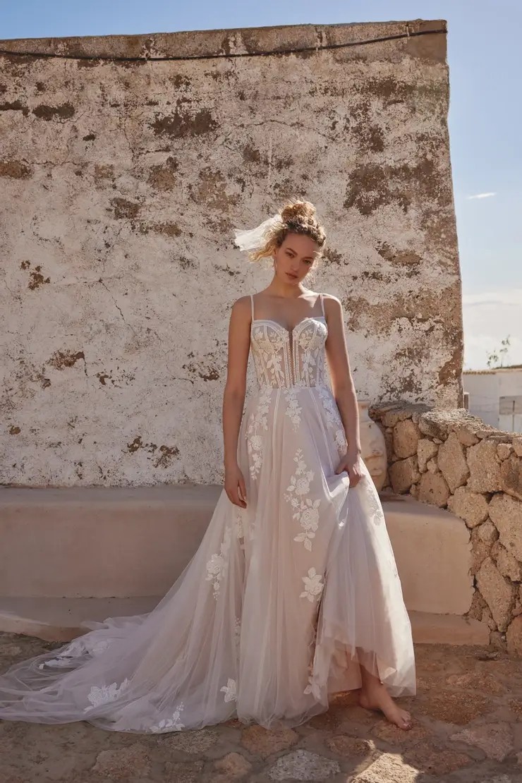 Model is wearing a wedding dress with a bikini neckline, beaded lace appliques, and a tulle chapel length train