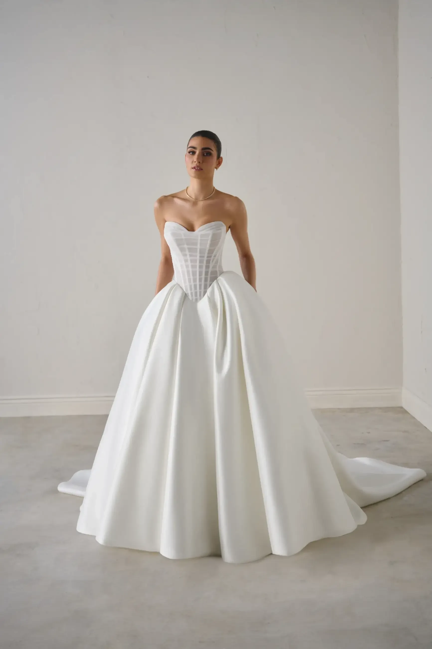 Model is wearing a mikado ball gown with a sheer tulle bodice and exposed boning
