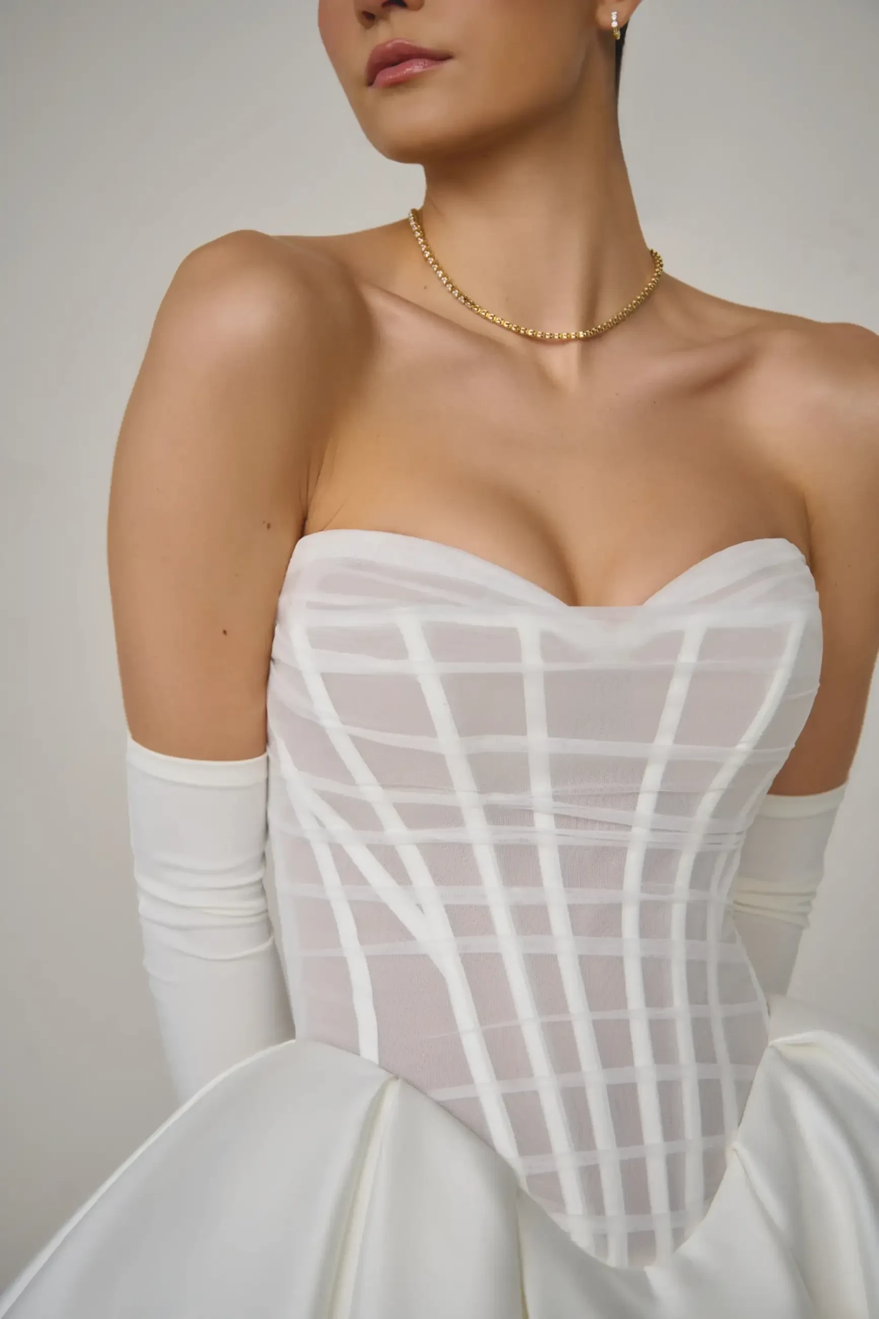 Model is wearing a mikado ball gown with a sheer tulle bodice and exposed boning