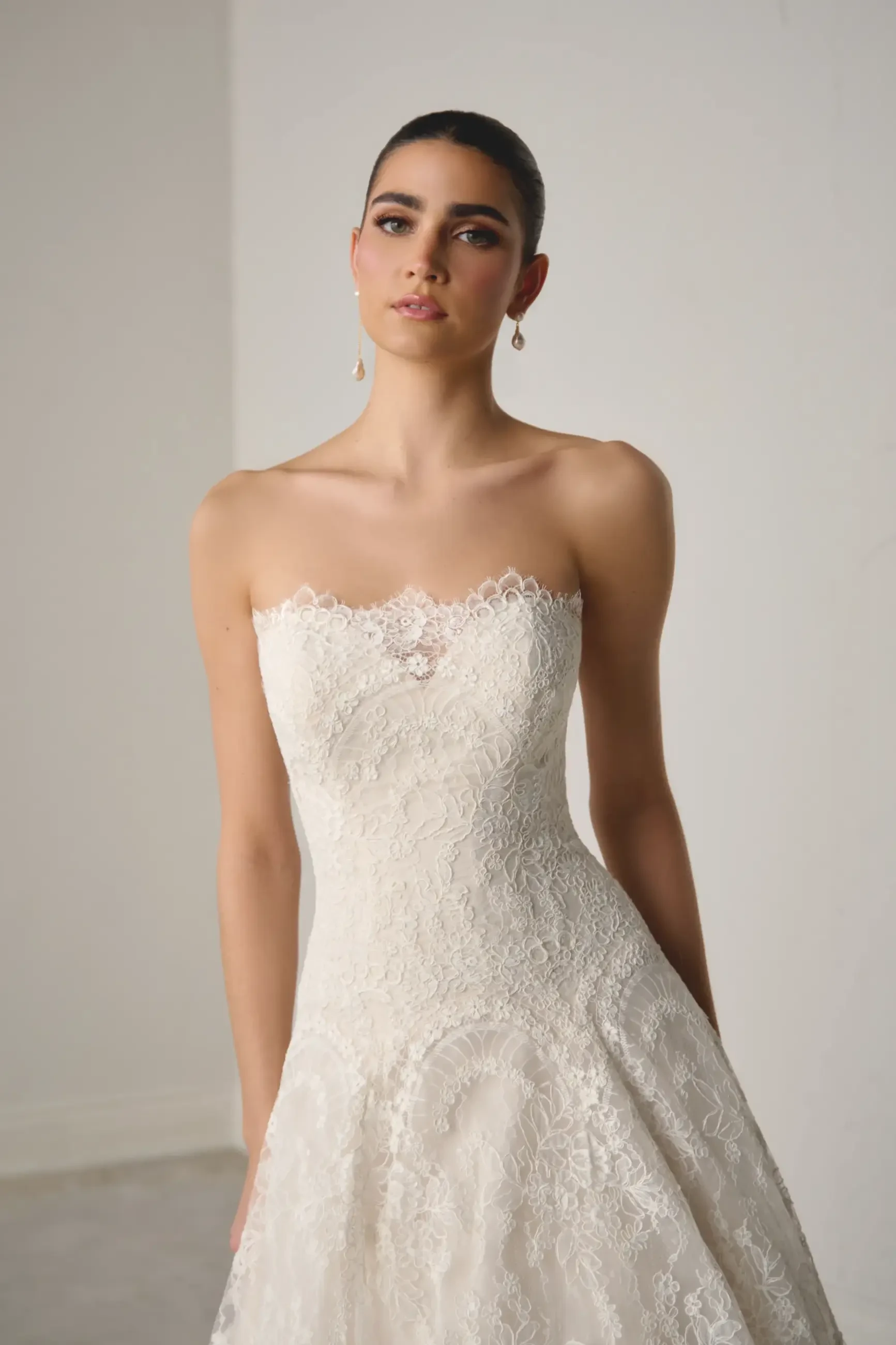 Model is wearing an allover lace a-line wedding dress with a dropped waist and straight neckline