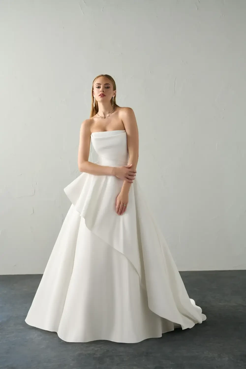 A woman in a strapless white gown stands against a neutral background.