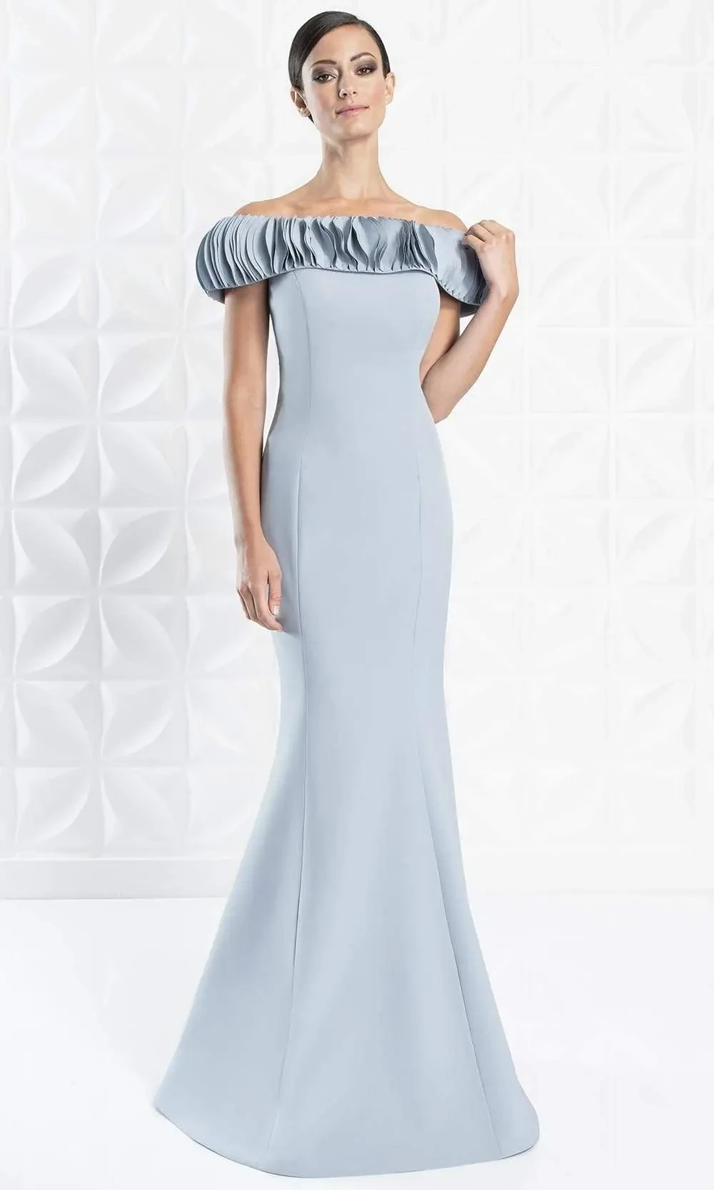 A woman in a light blue evening gown with a fitted silhouette and an off-the-shoulder ruffled neckline, standing against a textured white background.
