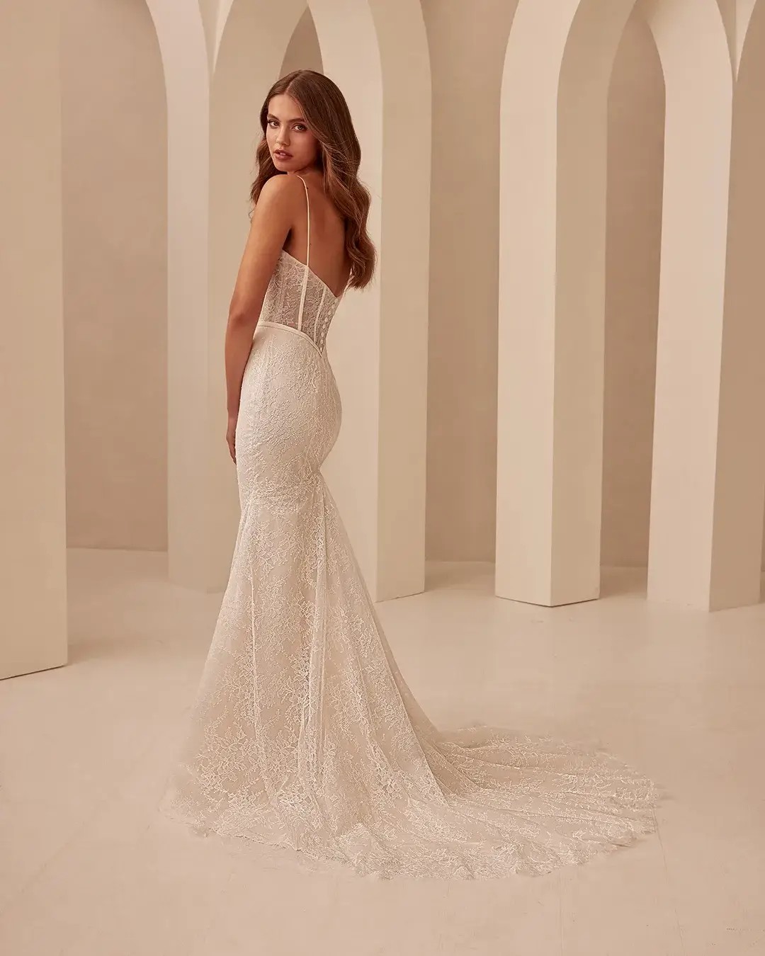 Model is wearing a fit and flare wedding dress with chantilly lace bodice and spaghetti straps 