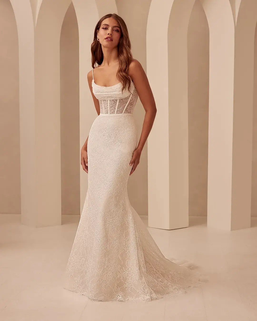 Model is wearing a fit and flare wedding dress with chantilly lace bodice and spaghetti straps 