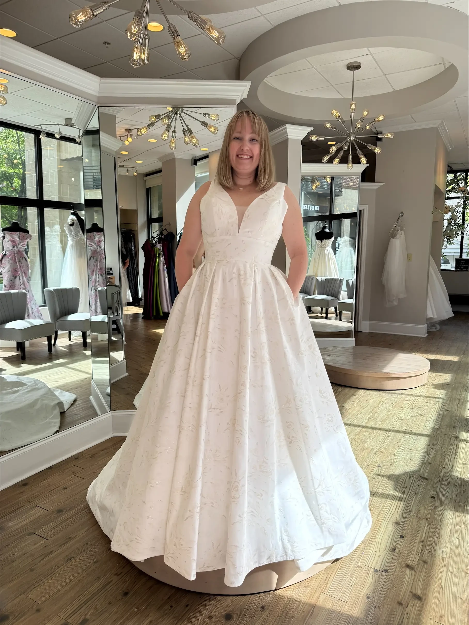 Model is wearing a sleeveless a-line bridal gown with a plunging neckline and embroidered fabric 