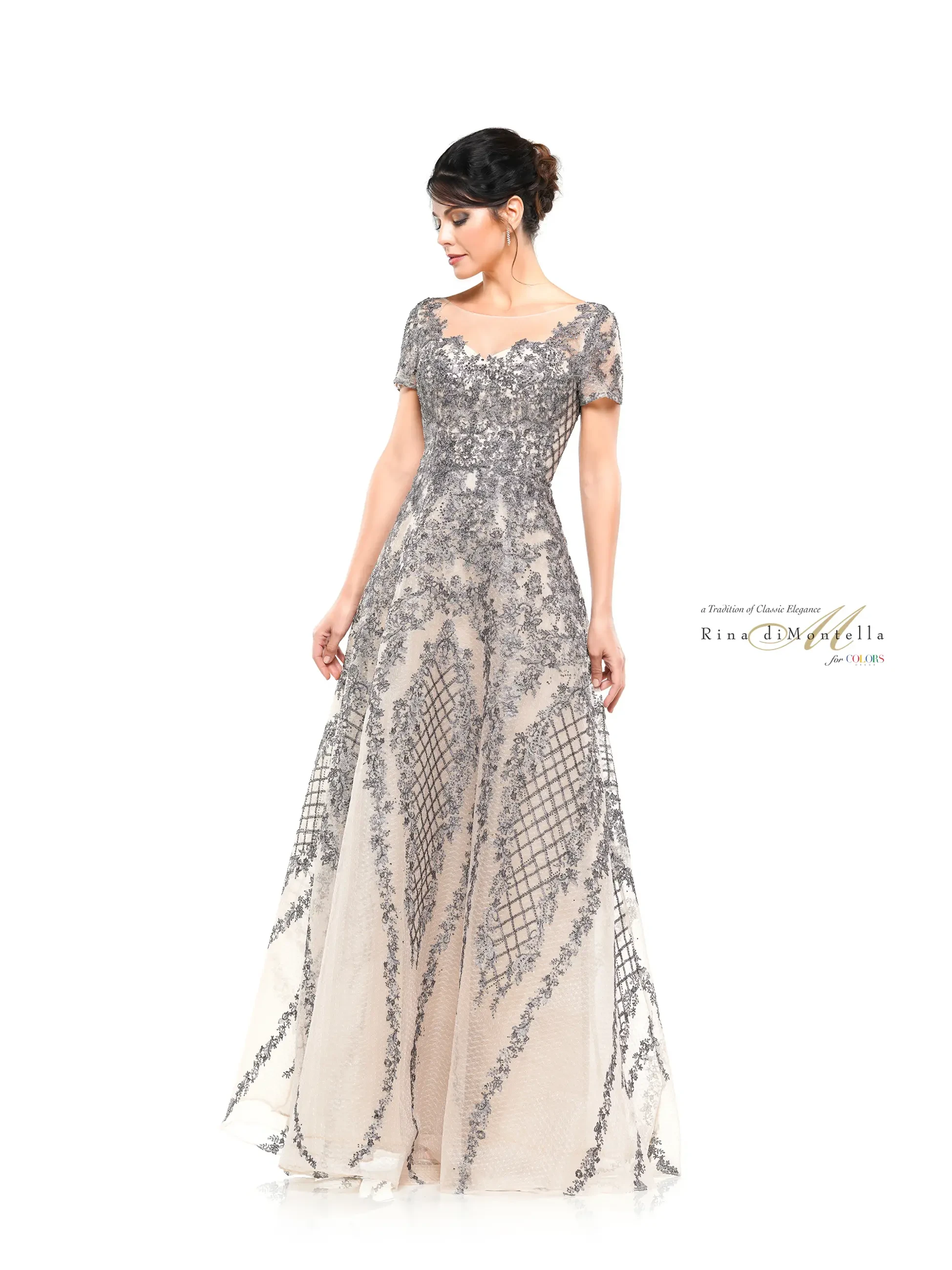 A woman in an elegant, intricately detailed silver and nude evening gown, standing gracefully with a slight pose.